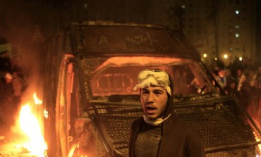 A protester stands in front of a burning riot police vehicle after it was seized in Cairo, Jan 28