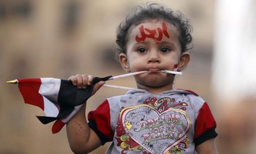 A girl with the colours of the Egyptian flag and the word "leave" painted on her face