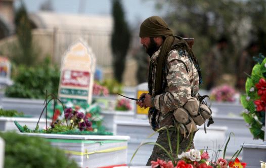 A Kurdish People's Protection Units (YPG) fighter walks near graves of fellow fighters during a visi