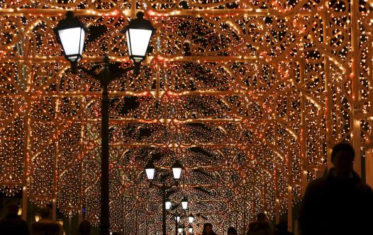 People walk along a street decorated with festive illumination lights, part of the New Year and Chri