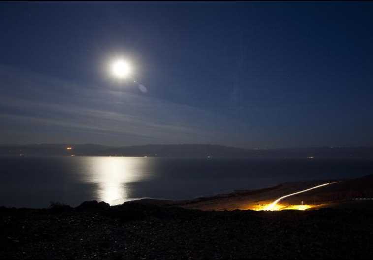 The moon shines in the night sky above the Dead Sea