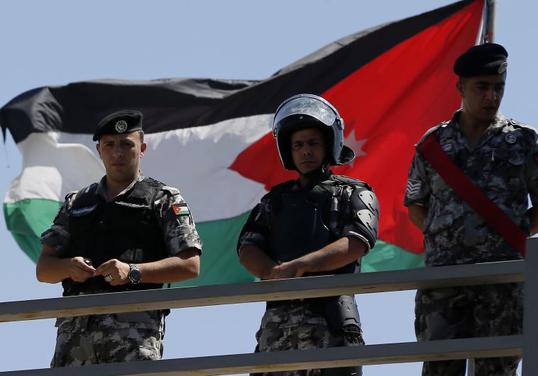 Jordanian riot police stand guard in front of a Jordanian flag as protesters hold a demonstration