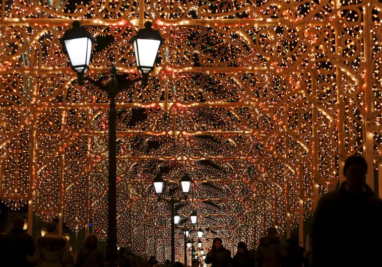 People walk along a street decorated with festive illumination lights, part of the New Year and Chri