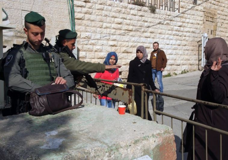 Border Police officers stop Palestinian women to check their belongings at a checkpoint in Hebron