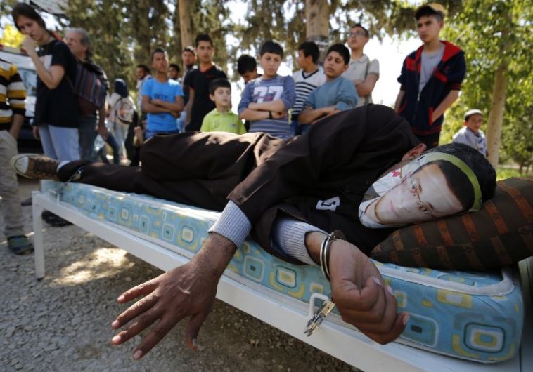 A Palestinian man in Ramallah lies on a bed wears a face covering depicting Mohammed al-Qiq