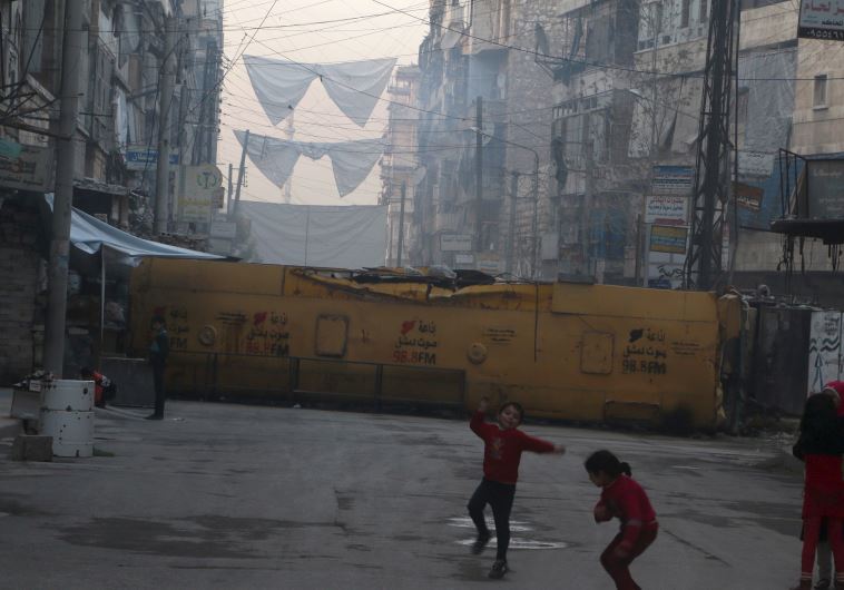 Children play near a bus barricading a street, which serves as protection from snipers loyal to Syri
