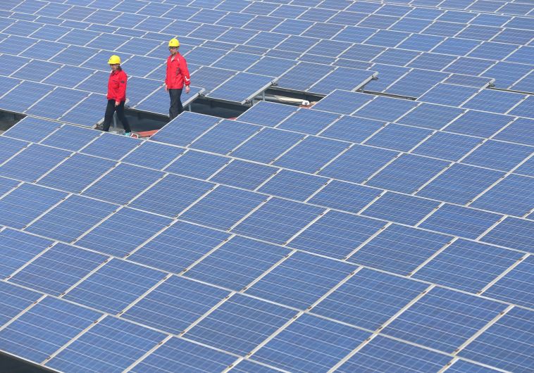 Workers walk past solar panels in Jimo, Shandong Province, China