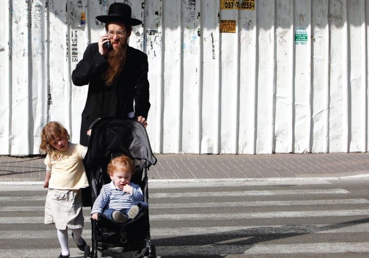 A MAN and his children cross the street in Bnei Brak while he speaks on his cellphone.