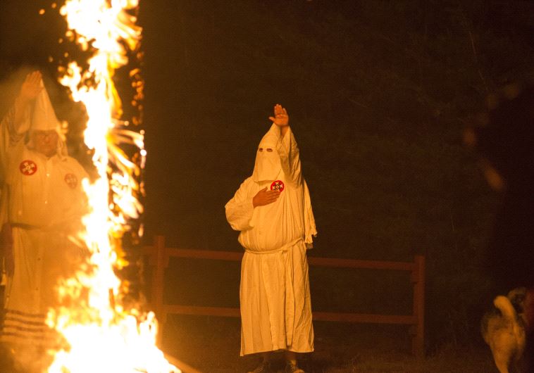 A member of the Ku Klux Klan salutes a lit cross during a cross lighting ceremony
