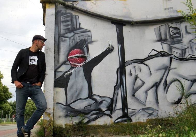 Teacher Christoph Glanz stands next to Palestinian slingshot graffiti. 