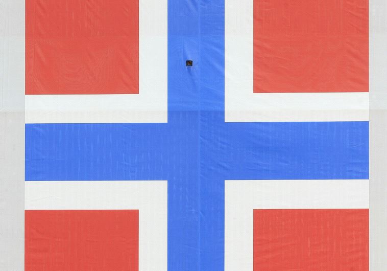 A woman cycles past a banner of the Norwegian flag attached to a warehouse in Oslo, Norway.