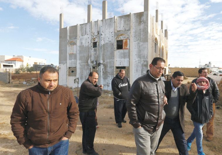 PEOPLE WALK past a building that was the site of clashes between Jordanian police and Islamist gunme