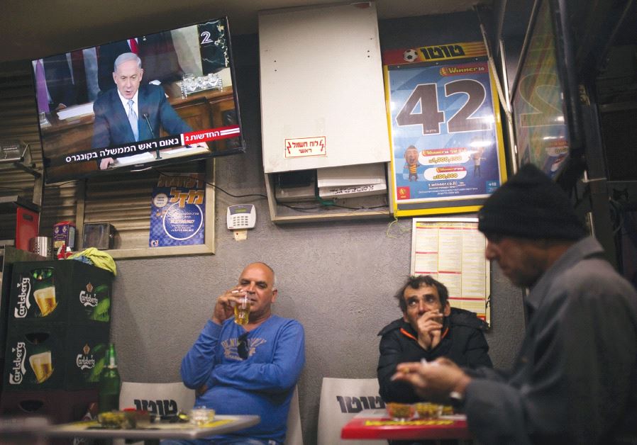PEOPLE SIT at a kiosk in Ashkelon as a television broadcasts Prime Minister Benjamin Netanyahu’s spe