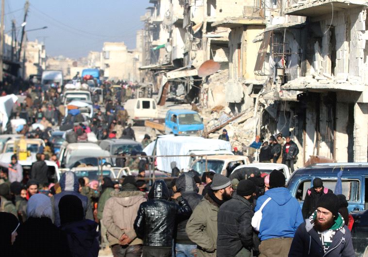 SYRIAN REBELS and civilians wait near damaged buildings to be evacuated from a rebel-held sector of 
