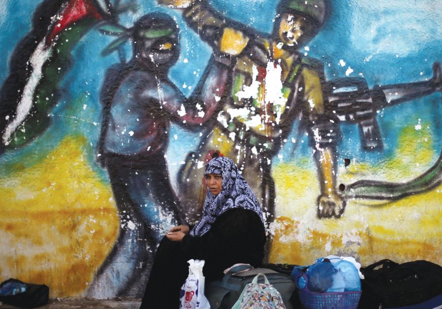 A WOMAN sits in front of a mural as she waits for a travel permit to cross into Egypt through the Ra