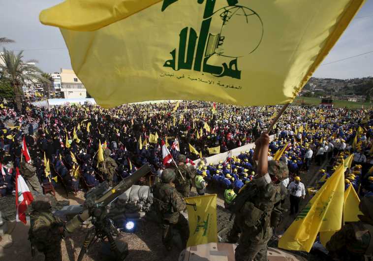 A Hezbollah member carries a Hezbollah flag while leader Hassan Nasrallah talks on a screen 