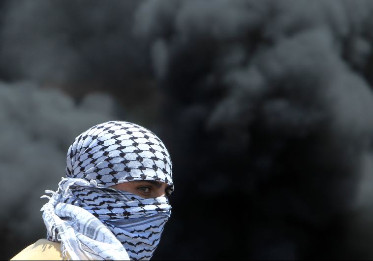A masked Palestinian protester looks on amid the smoke of burning tires during clashes with IDF
