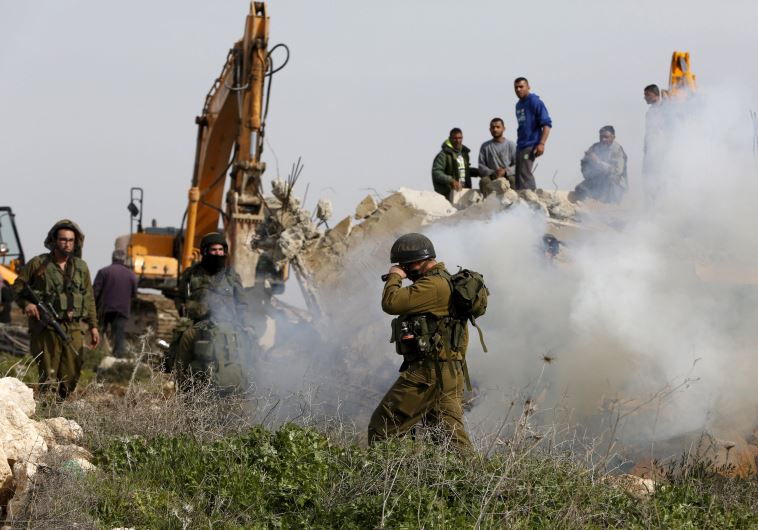 An Israeli soldier reacts to tear gas during the demolition of a Palestinian house