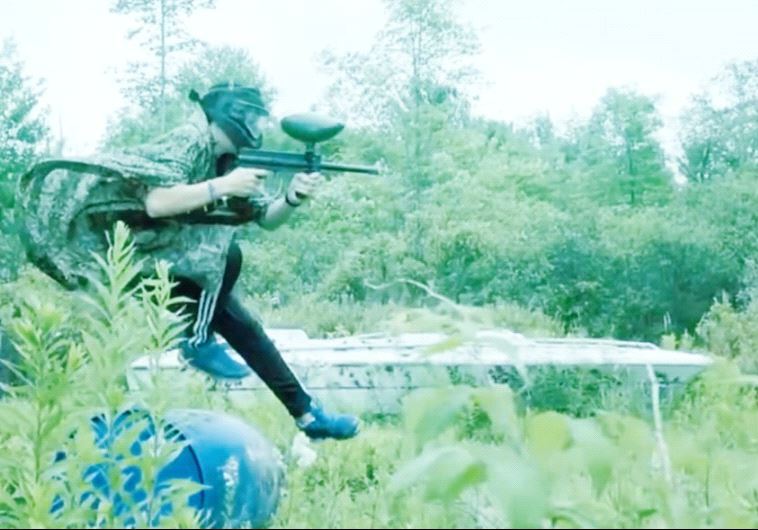 A SCREENSHOT of the video depicts teenagers holding paintball guns and running in a forest through a