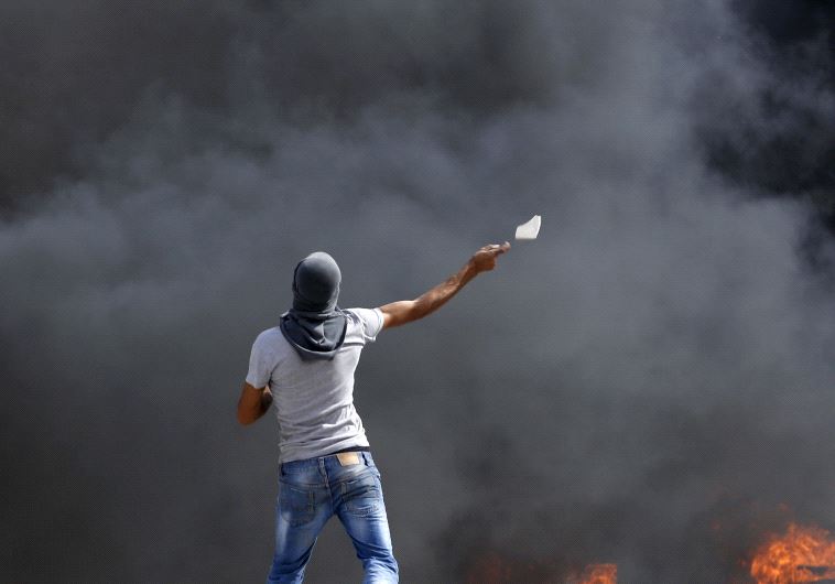A Palestinian throws a stone towards Israeli troops during clashes at Qalandia checkpoint