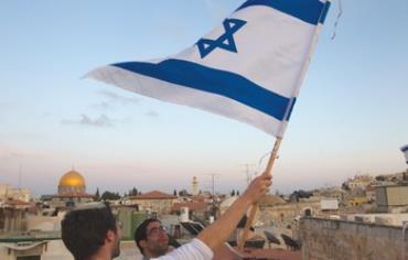 A JEWISH man waves a flag with the Temple Mount in the background.