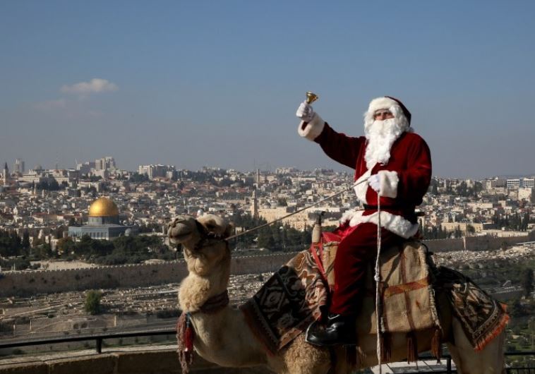 A Christian Palestinian man dressed up as Santa Claus rings a bell as he sits on a camel
