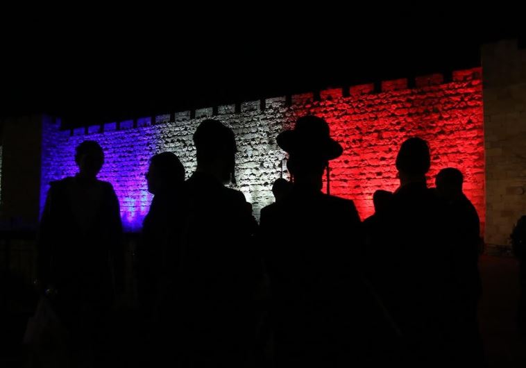 Jerusalemites look on as the colors of the French flag light up the Old City walls