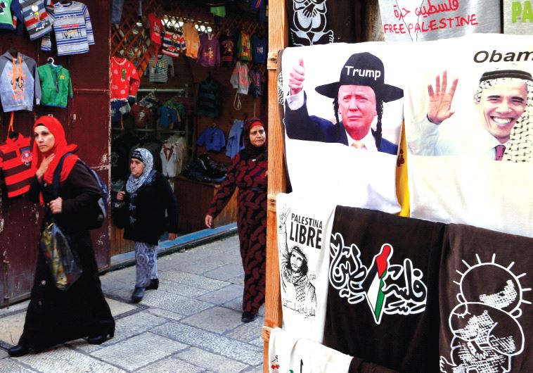 Arab women walk past a shop in Jerusalem’s Old City displaying T-shirts with images of newly elected