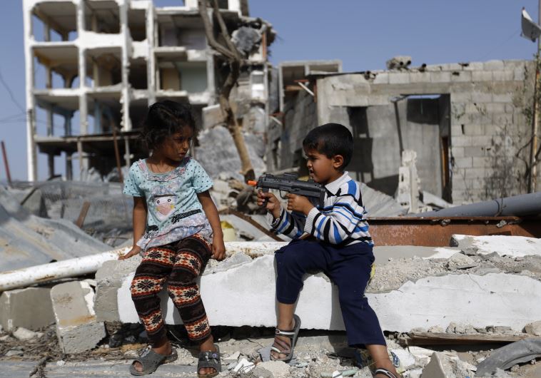 Palestinian children play with a toy gun in front of homes ruined during Operation Protective Edge