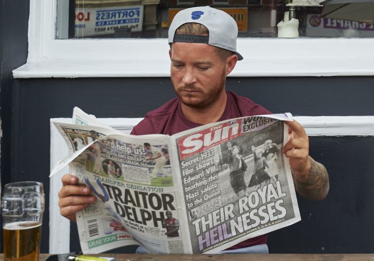 A man reads The Sun showing photo of the young Queen Elizabeth II giving Nazi salute. 