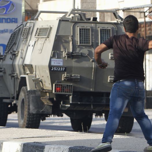 A Palestinian youth hurls stones at Israeli troops during clashes in Nablus