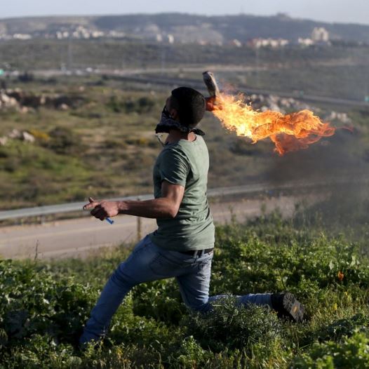A Palestinian protester hurls a Molotov cocktail towards Israeli troops during clashes