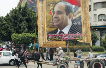 Man on a horse-drawn cart rides past banner depicting  Abdel Fattah al-Sisi in Cairo