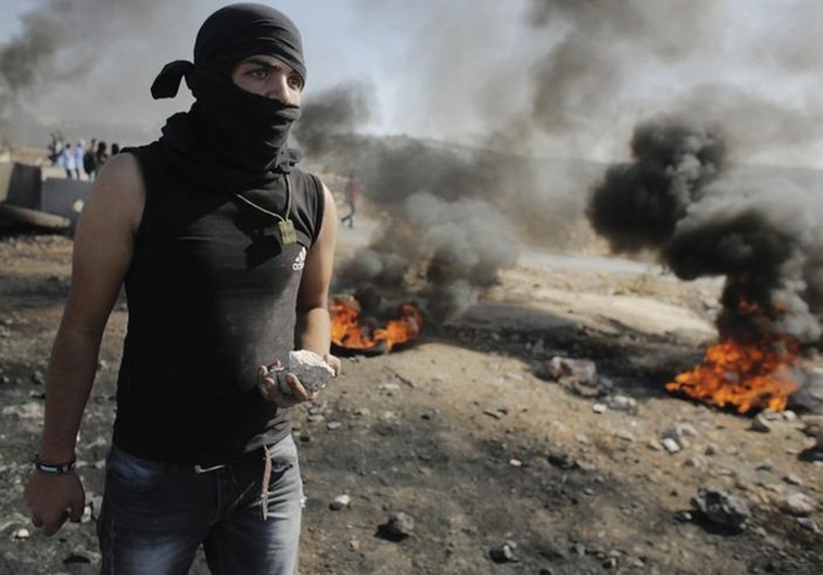 Youth holds stone as Palestinians clash with IDF in the West Bank
