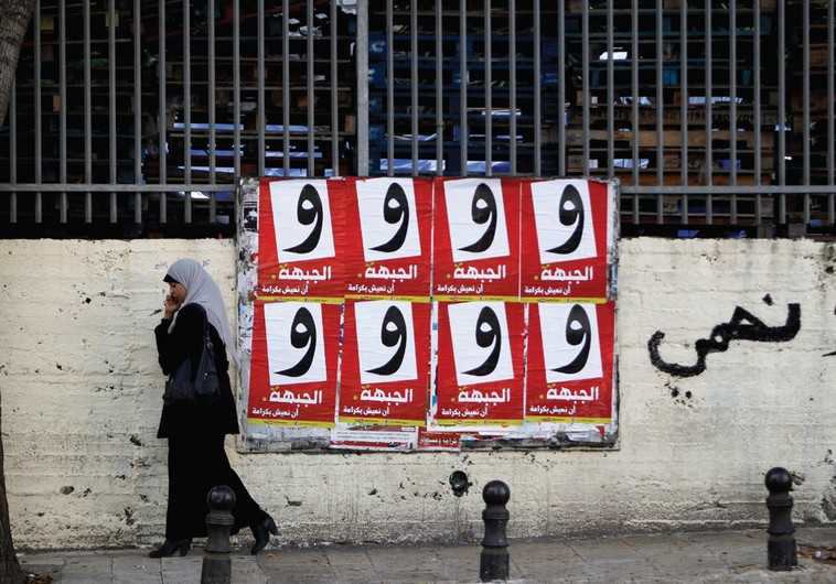 A WOMAN walks past campaign posters for the Arab-led Hadash party in Umm al-Fahm
