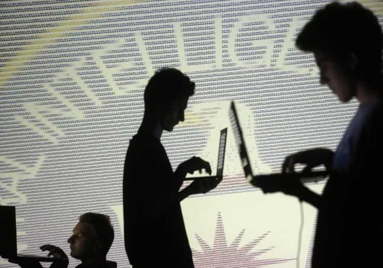 People are silhouetted as they pose with laptops in front of a screen projected with the CIA emblem