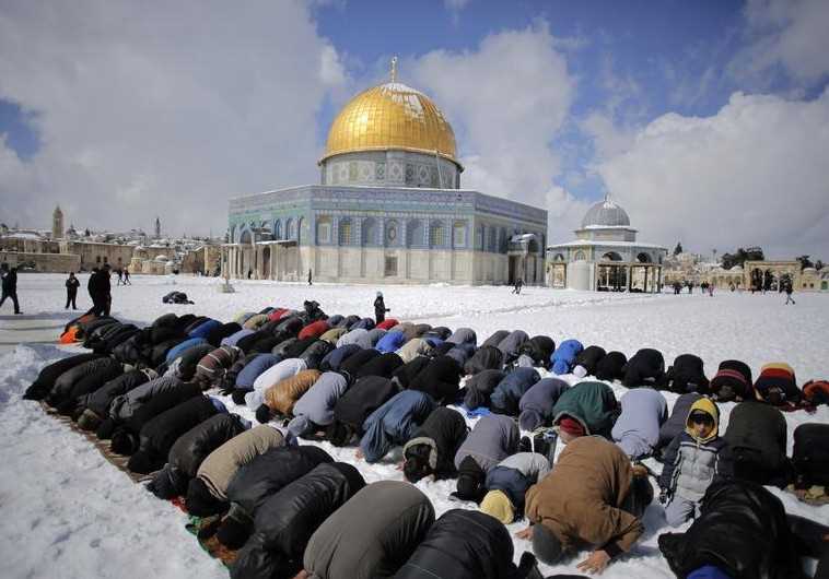 Palestinian men pray in front of the snow-covered Dome of the Rock in Jerusalem's Old City