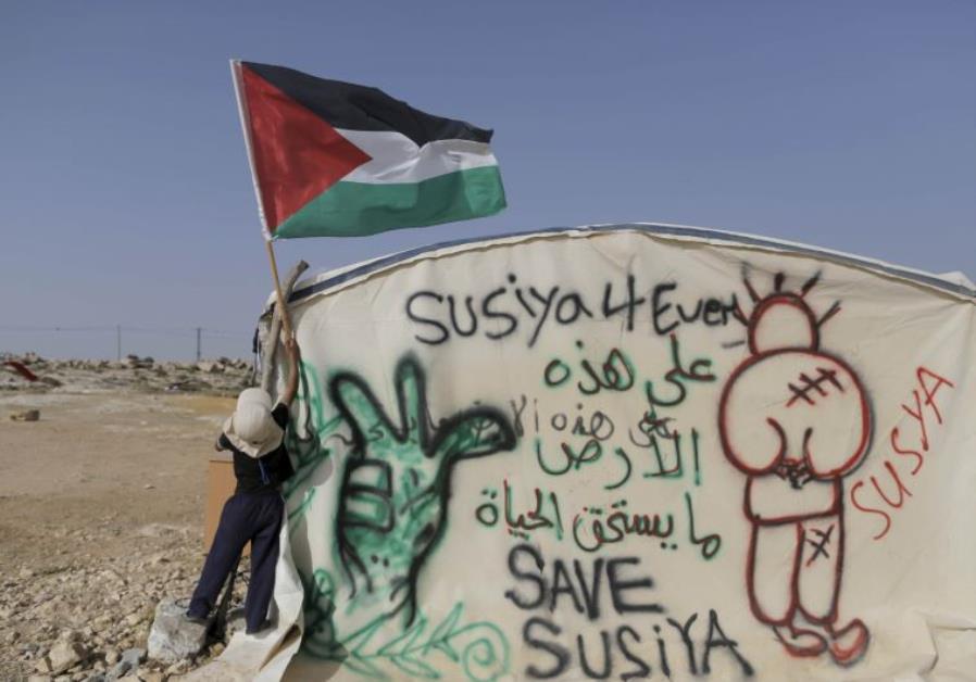 A Palestinian boy places a Palestinian flag on a tent in the West Bank village of Sussiya