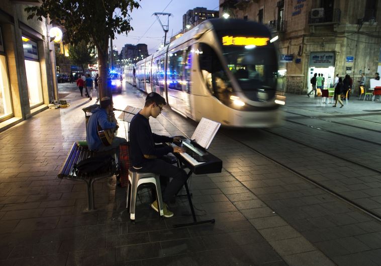 Israeli teens play music as a light rail tram passes by in Jerusalem