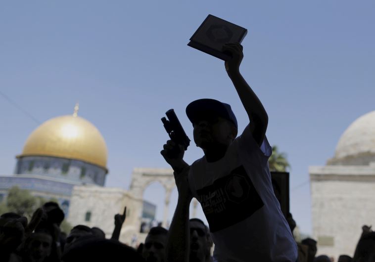 A Palestinian youth is silhouetted as he holds a toy gun and a Koran during a protest