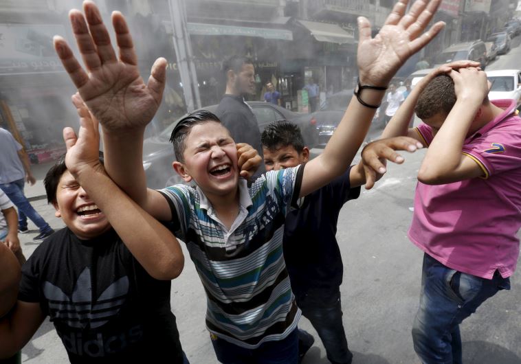 Children react as personnel from the Greater Amman Municipality spray them with a water sprinkler