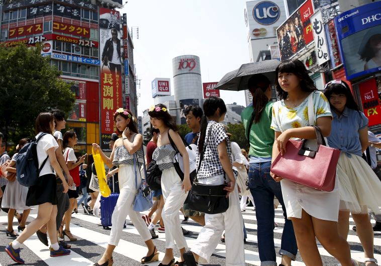 People cross a junction in front of advertising billboards in the Shibuya shopping district in Tokyo