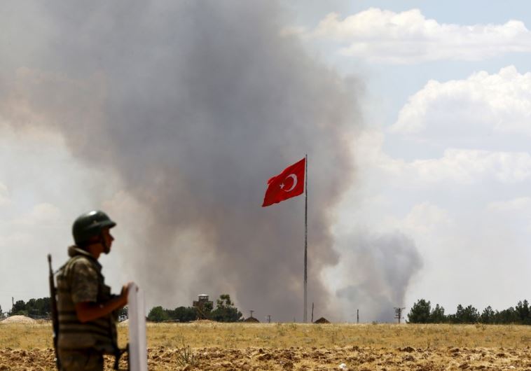 A Turkish soldier stands guard while smoke rises in the Syrian town of Kobani 