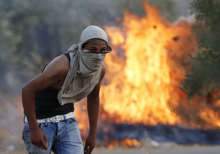 A Palestinian stone-thrower looks on as he stands in front of a fire during clashes with IDF troops 