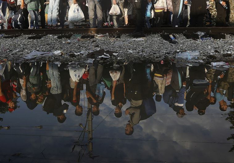 Syrian refugees are reflected in a puddle as they wait for their turn to enter Macedonia 