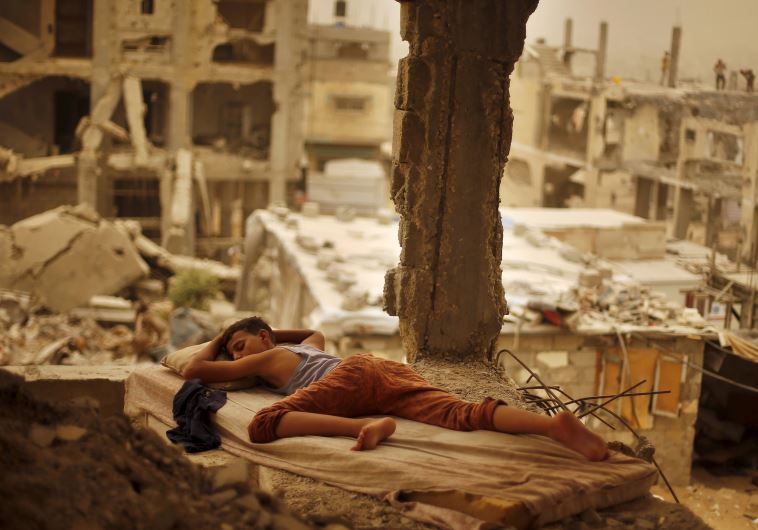 A Palestinian boy sleeps on a mattress inside the remains of his family's house