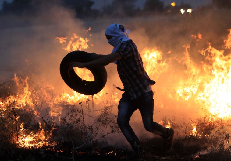 A Palestinian protester throws a tire into a fire during clashes with Israeli security forces