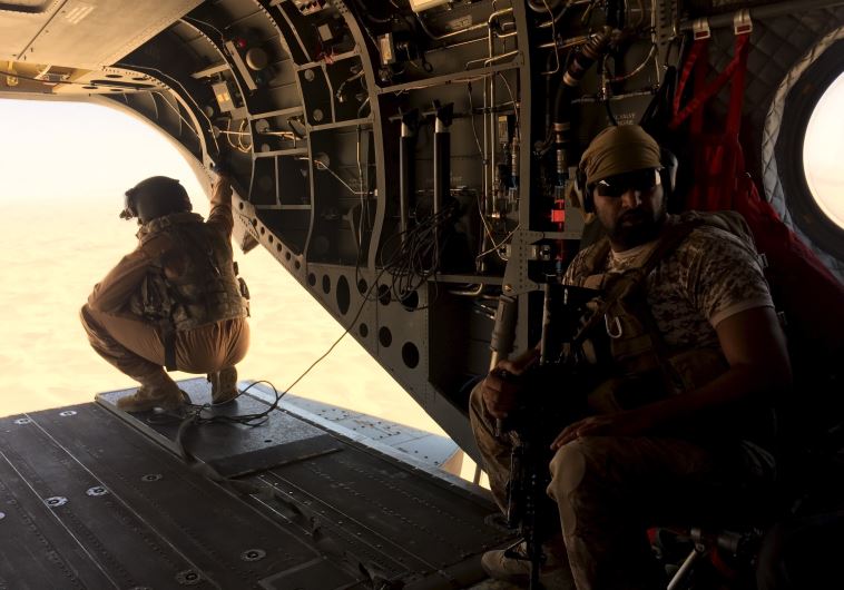 A soldier and an airman from the United Arab Emirates sit in a helicopter flying a small group of jo