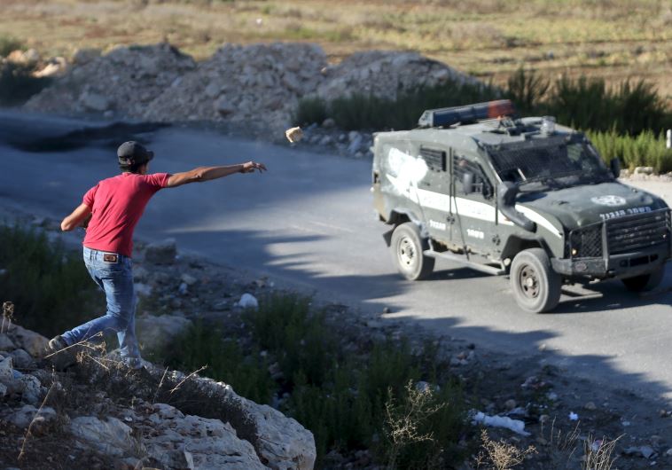 A Palestinian throws a stone at a Border Police vehicle during a protest near Ramallah
