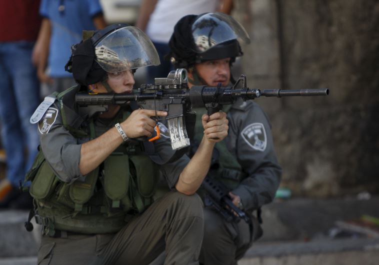 An Israeli border policeman aims his weapon at Palestinians during clashes in Hebron